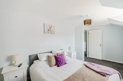 a white bedroom with a bed with purple pillows at Auchenlarie Courtyard No 1 in Gatehouse of Fleet