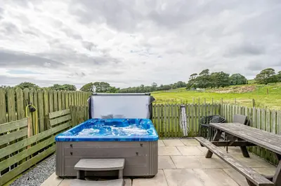 a hot tub sitting on a patio next to a wooden fence at Auchenlarie Courtyard No 4 in Gatehouse of Fleet