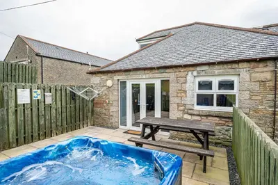a hot tub and a picnic table in front of a house at Auchenlarie Courtyard No 2 in Gatehouse of Fleet