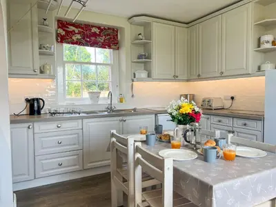 a kitchen with white cabinets and a table with flowers on it at Kirk House Longtown, ideal for groups or families holidaying together in Longtown