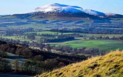 a snow covered mountain in a green field with a mountain at Dungavel Cottage in Roberton