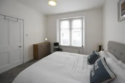 a bedroom with a large white bed and a window at Hunter Links Cottage in Prestwick