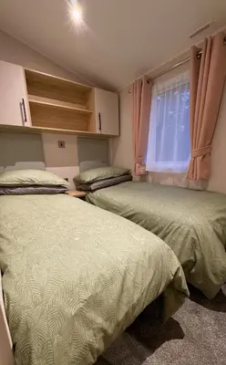 a bedroom with two beds and a window with pink curtains at Carlisle CAMELOT HOLIDAY PARK CA65SZ MANOR in Longtown