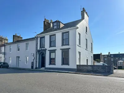 a white house sitting on the side of a street at The Manor - Beachwalk Apartments in Ayr