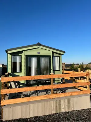 a green tiny house with a wooden deck at Maneight Fir View with hot tub in Dalleagles