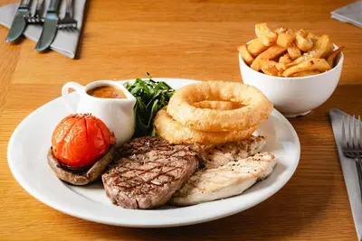 a plate of food with meat and onion rings and french fries at The Kellbank in Gosforth