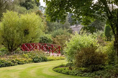 a path in a garden with a red bridge at Dabton House in Carronbridge