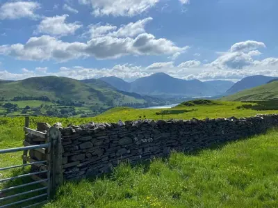 a stone wall in a field with mountains in the background at Rhodes Retreat, Lake District in Brigham