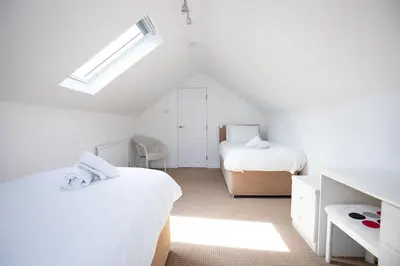 a white bedroom with two beds and a window at SHELTER STONE - Cottage in the heart of the Lakes in Keswick