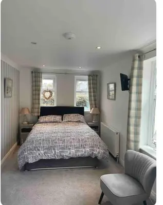 a bedroom with a bed and a chair and windows at Beach room in Ayr