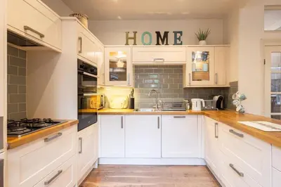 a kitchen with white cabinets and a home sign on the wall at Hampton Manor House - 9 Bedrooms in St Bees