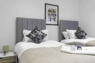 two beds in a hotel room with white sheets and pillows at Strath Apartment in Strathaven