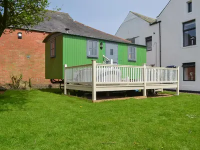 a green and white house with a wooden deck at Sian's Shepherds Hut - Uk43561 in Bowness-on-Solway
