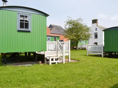 a green house and two benches in a yard at Sian's Shepherds Hut - Uk43561 in Bowness-on-Solway