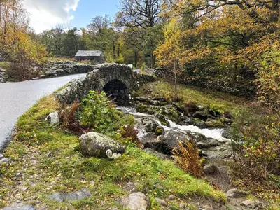 a stone bridge over a stream next to a road at Coast To Coast Cottage in Cleator Moor