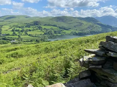 a stone wall on a grassy hill with a lake at Stanleys Sanctuary, Lake District in Plumbland