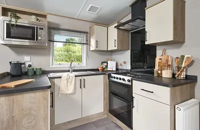 a kitchen with white cabinets and a stove top oven at Queensberry Bay Essential Clover Caravan Pet in Annan