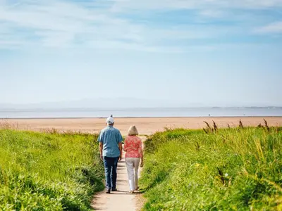 a man and woman walking down a path towards the beach at Queensberry Bay Essential Clover Caravan in Annan