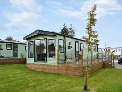 a green tiny house with a deck in a yard at Regal Lodge in Plumbland