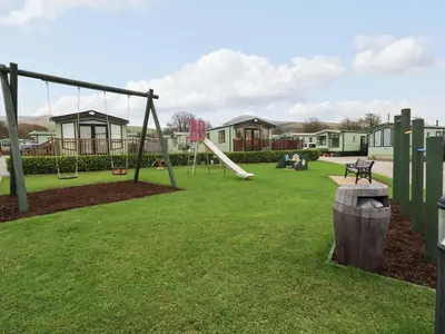 a playground with a slide and a swing at Highlands Way Lodge in Workington