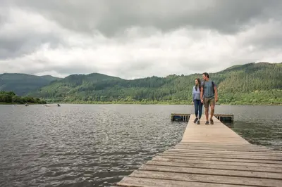 a man and woman standing on a dock on a lake at Lodge by the Lake - Lake District - Hot Tub in Bassenthwaite