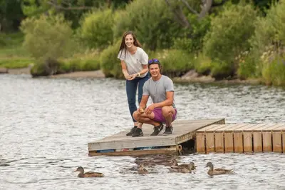 a man and a woman standing on a dock with ducks at Lodge by the Lake - Lake District - Hot Tub in Bassenthwaite