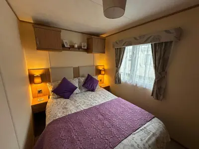 a bedroom with a bed with purple pillows and a window at The Cosy Hedgerow in Port Carlisle