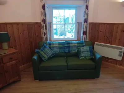 a living room with a green couch and a window at The Dairy - Patterdale Hall in Penrith
