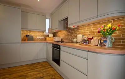 a kitchen with white cabinets and a brick wall at Edenville Cottage in Gatehouse of Fleet