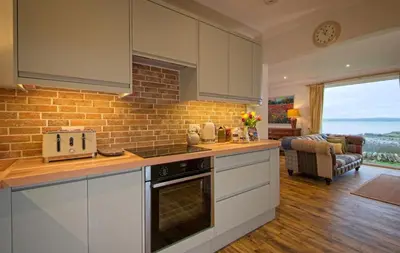 a kitchen with white cabinets and a brick wall at Edenville Cottage in Gatehouse of Fleet