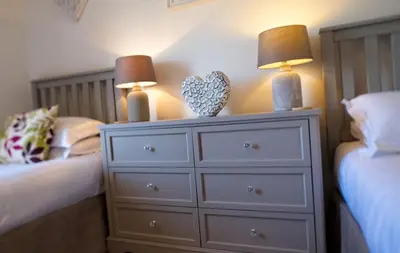 a bedroom with two beds and a dresser with two lamps at Edenville Cottage in Gatehouse of Fleet