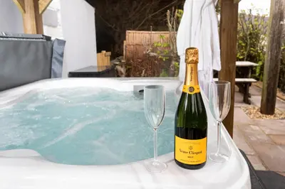 a bottle of champagne and two wine glasses next to a hot tub at Scenery Hill Hideaways The Coach House Charming Retreat with Jacuzzi and BBQ Hut Near the Lake District in Workington
