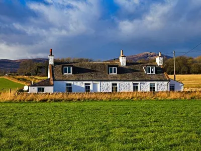 a white house with a black roof in a field at Arthur's Cottage in Dumfries
