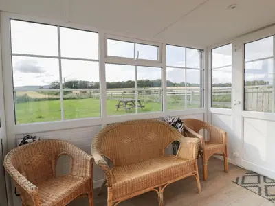 a screened in porch with wicker chairs and windows at Arthur's Cottage in Dumfries