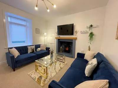 a living room with blue couches and a fireplace at Beautifully Presented Cosy Town Centre Cottage - Pass the Keys in Dumfries