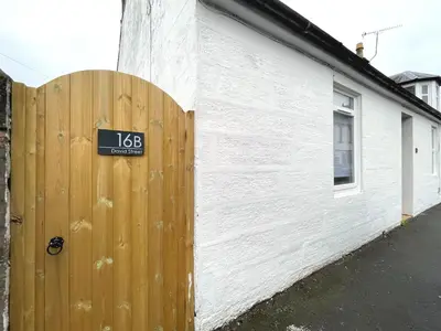 a wooden fence with a sign on it next to a building at Beautifully Presented Cosy Town Centre Cottage - Pass the Keys in Dumfries