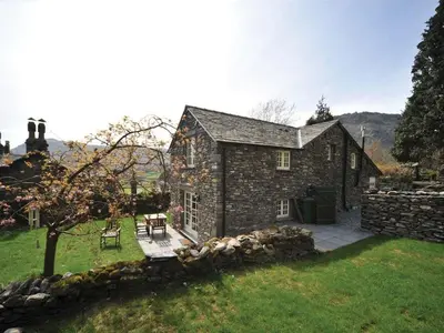 an old stone house with a patio in a yard at Stone Arthur Cottage in Ambleside