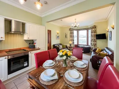 a kitchen and living room with a wooden table and red chairs at South Haven in Portpatrick