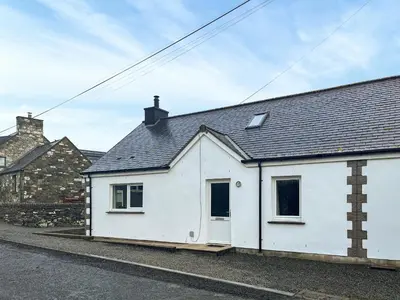 a white house with a black roof on a street at Flo's Cottage in Eldrig Village