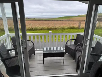 a porch with chairs and a table and a view of a field at The Retreat - Turnberry Holiday Park Amazing Sea View in Girvan