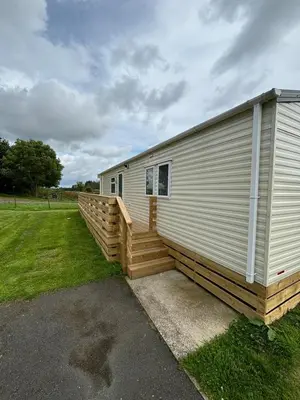 a large white building with a wooden deck next to a field at 131 Loch View Three Lochs Holiday Park in Newton Stewart