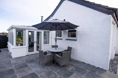 a table and chairs with an umbrella on a patio at Hidden Hive in Gretna