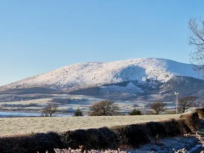 a mountain covered in snow on top of a field at Beautiful Countryside Lodge with Outstanding Views - Pass the Keys in Dumfries