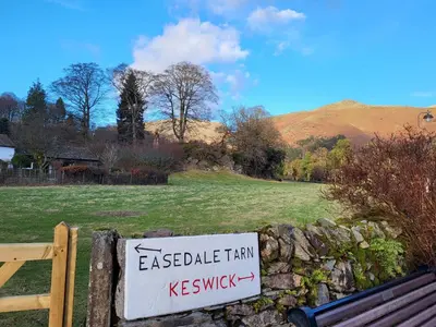 a sign on a stone wall next to a field at Holly Cottage Grasmere in Grasmere