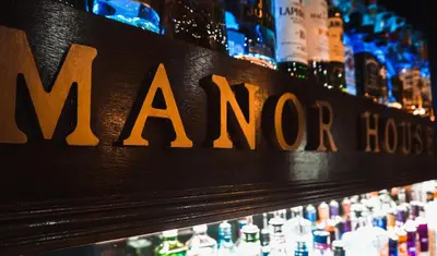a sign for a bar with bottles of alcohol at Manor House Hotel, Cockermouth in Cockermouth
