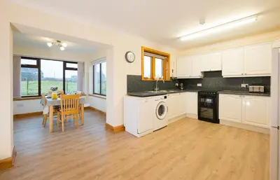 a kitchen with white cabinets and a table and a dining room at Shellhill Cottage at Clauchan Holiday Cottages in Gatehouse of Fleet
