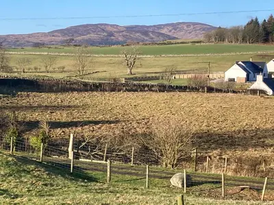 a farm with a fence in a field at Shellhill Cottage at Clauchan Holiday Cottages in Gatehouse of Fleet
