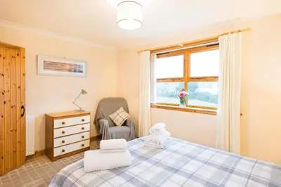 a bedroom with a bed and a chair and a window at Shellhill Cottage at Clauchan Holiday Cottages in Gatehouse of Fleet
