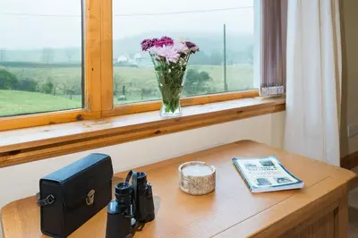 a desk with a vase of flowers and a window at Shellhill Cottage at Clauchan Holiday Cottages in Gatehouse of Fleet