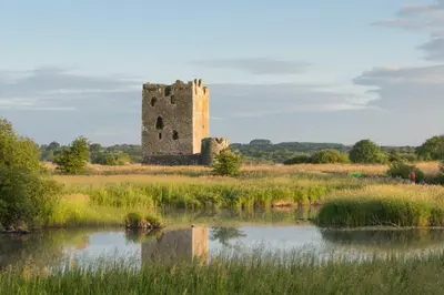 a castle sitting in a field next to a body of water at Mains of Greenlaw Cottage in Castle Douglas